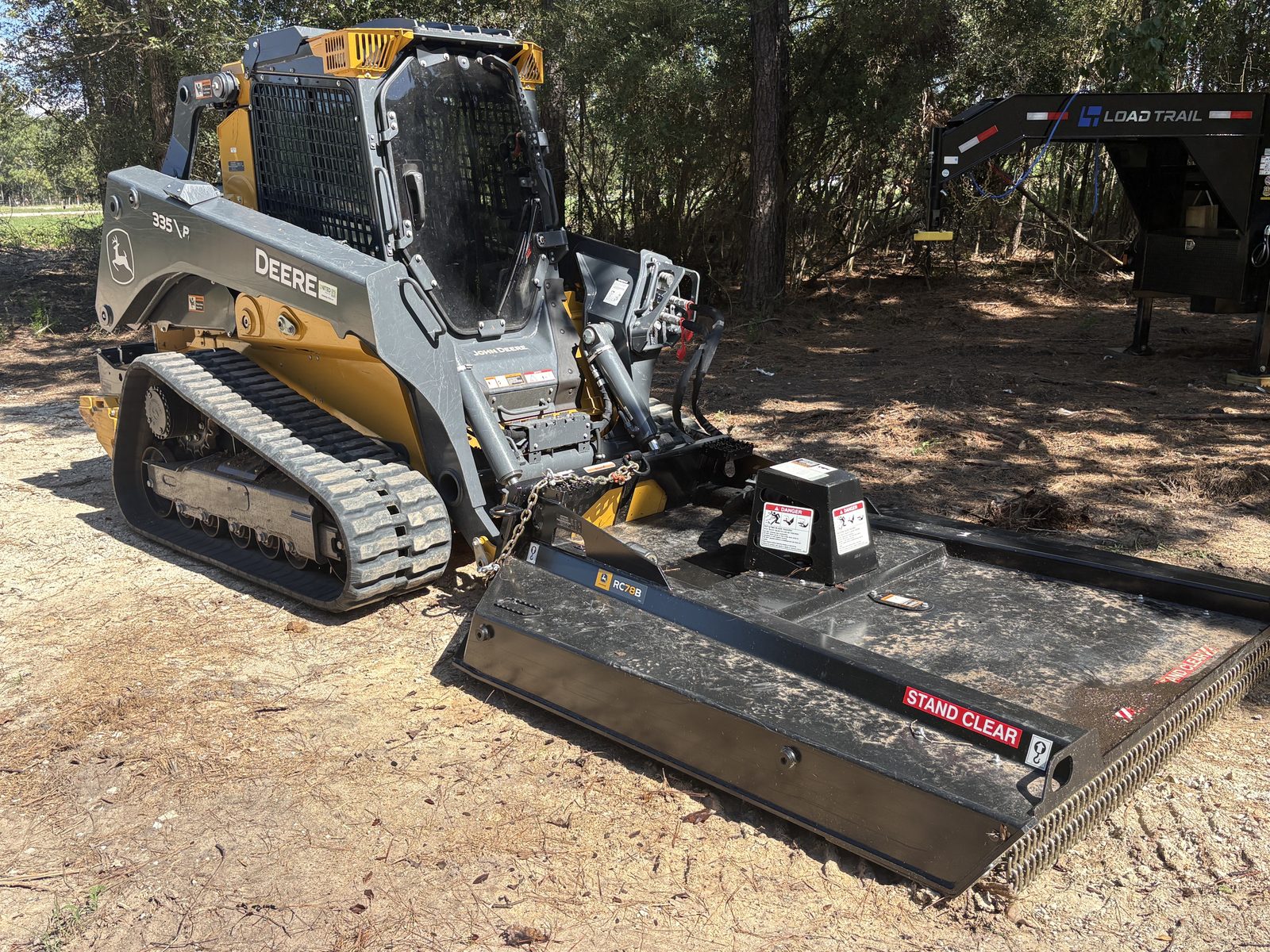 John Deere 335P skid steer with rotary cutter mowing attachment on a job site